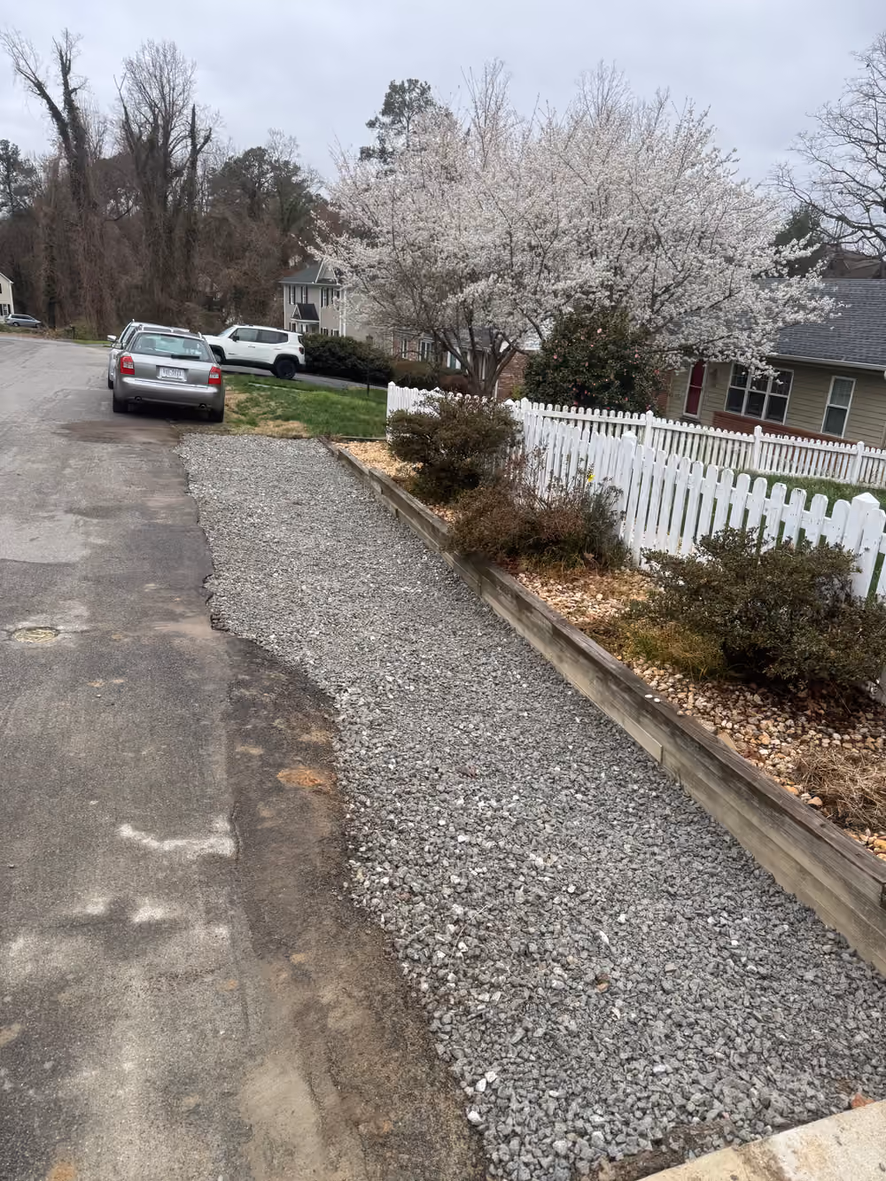 Refreshed gravel driveway beside a white picket fence and flowering cherry tree