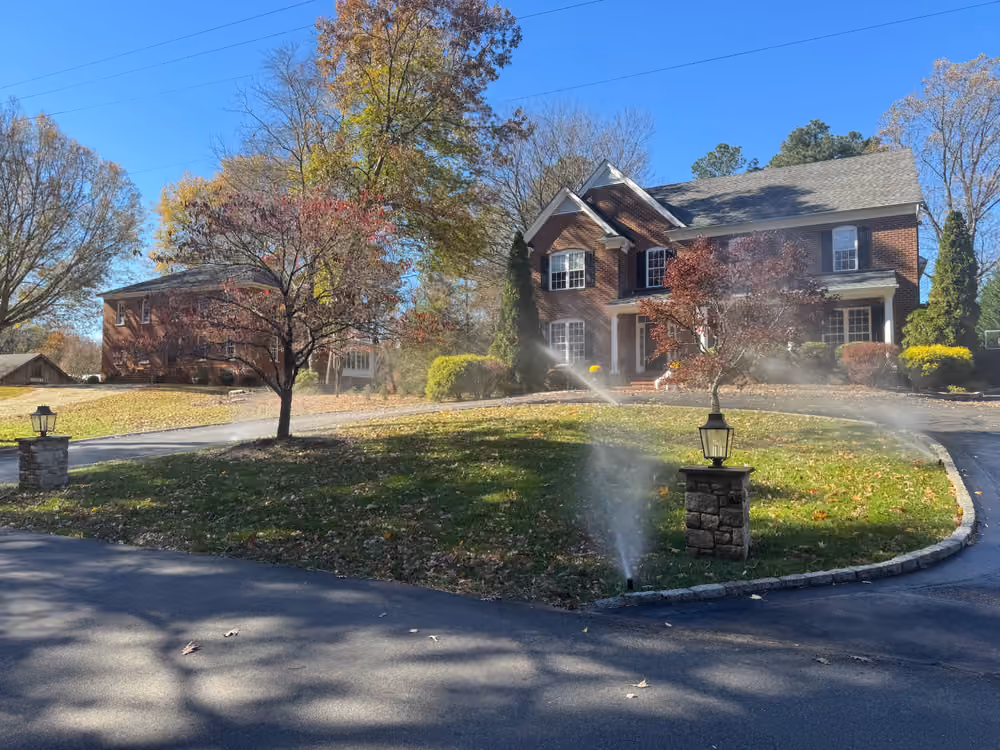 Irrigation heads running on a front lawn beside the driveway of a brick home
